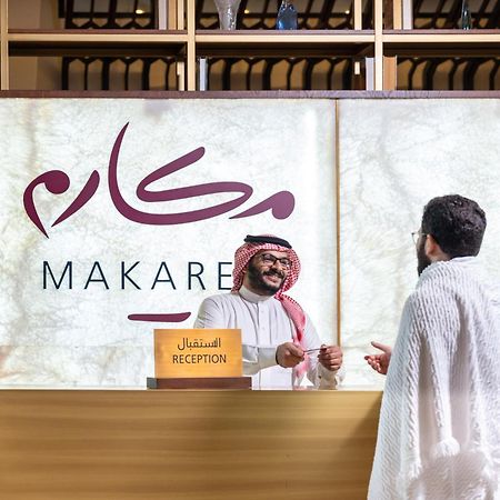 Makarem Ajyad Makkah Hotel Мекка Экстерьер фото The photo depicts a reception area in a hotel or establishment named "Makarem." In the image, a receptionist, dressed in traditional attire, is smiling and interacting with a guest who is wearing a white robe, commonly known as a thobe or ihram. The 