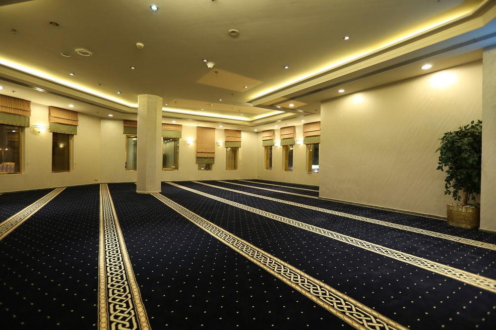 Makarem Ajyad Makkah Hotel Мекка Экстерьер фото The photo shows a spacious indoor area with a plush blue carpet featuring a decorative pattern. The room is well-lit, with soft lighting along the ceiling. There are several windows, allowing natural light to enter, and a few plants are positioned ar