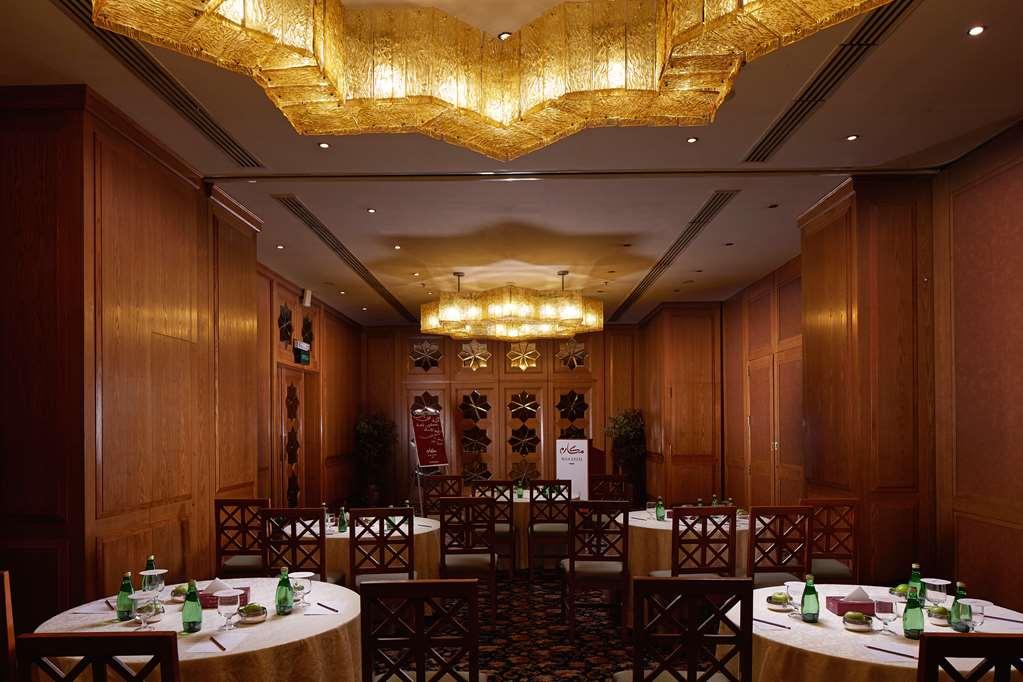 Makarem Ajyad Makkah Hotel Мекка Удобства фото The photo shows a well-decorated dining room with wooden paneling and elegant furnishings. There are round tables covered with tablecloths, and each table is arranged with glasses of water. The lighting is warm, provided by elaborate chandeliers on t