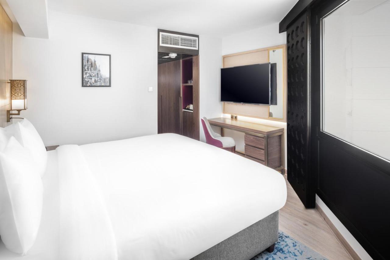 Makarem Ajyad Makkah Hotel Мекка Экстерьер фото The photo shows a modern hotel room featuring a large bed with white linens at the forefront. In the background, there is a wall-mounted television across from a desk with a chair. A wardrobe or cabinet is located to the side, and there's a decorativ