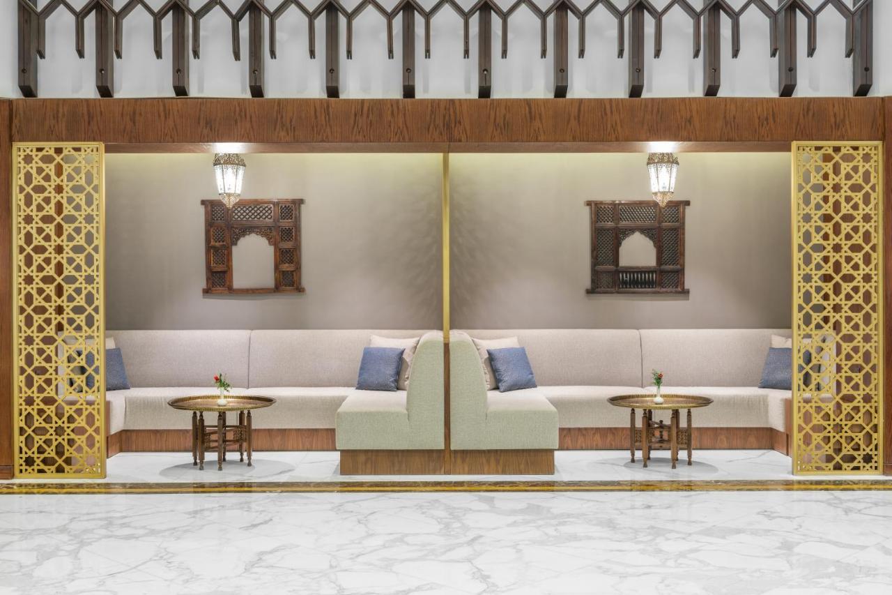 Makarem Ajyad Makkah Hotel Мекка Экстерьер фото The photo depicts a modern, elegantly designed seating area. It features a pair of sofas with light-colored upholstery, accented by blue cushions. There are several small tables in front of the sofas, likely meant for drinks or decorative items. The 