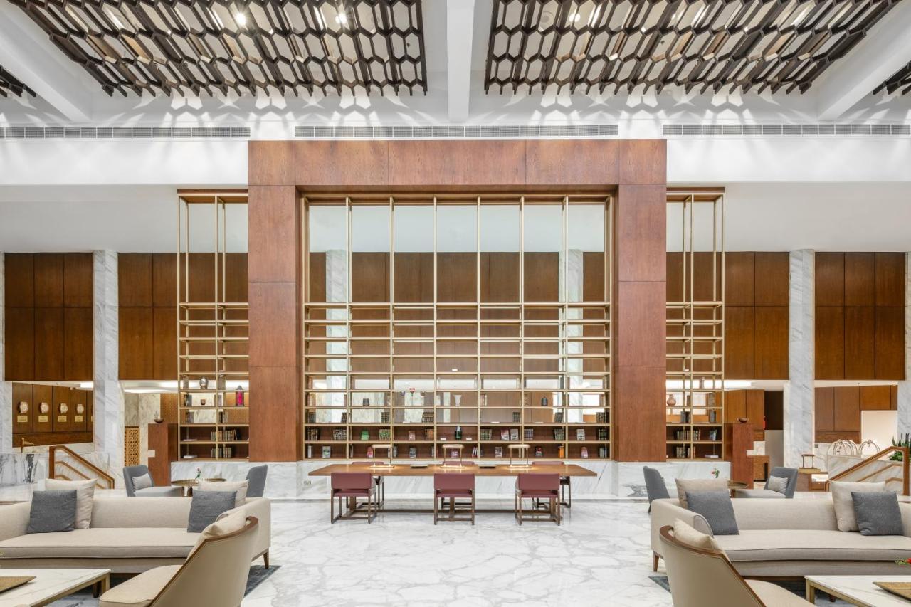 Makarem Ajyad Makkah Hotel Мекка Экстерьер фото The photo shows a spacious interior of a modern lobby or lounge. The design features a large wooden structure with a grid-like pattern in the center, possibly serving as a decorative partition. The walls are adorned with brown wooden panels, and marb