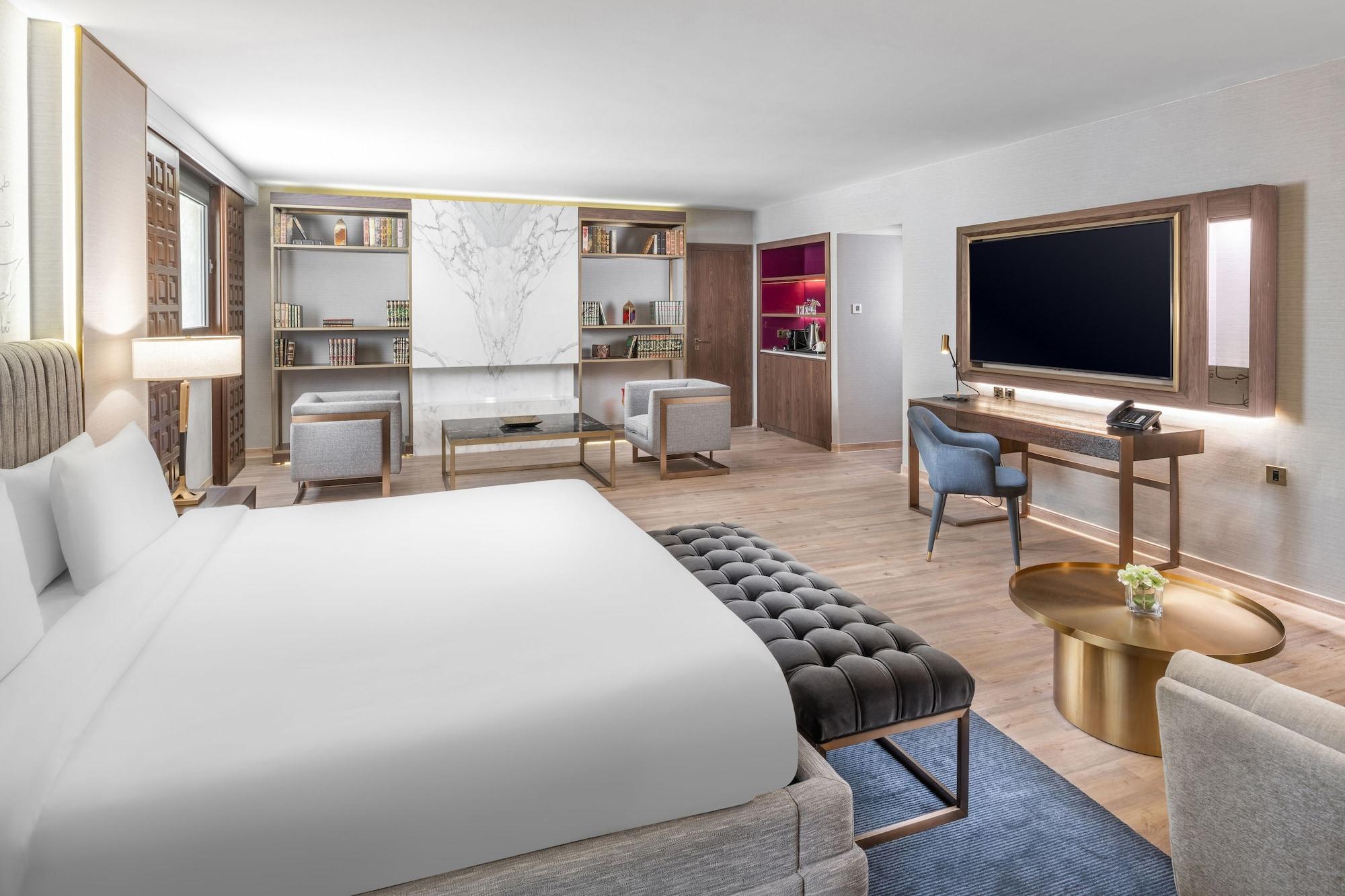 Makarem Ajyad Makkah Hotel Мекка Экстерьер фото The photo shows a modern hotel room designed with a contemporary aesthetic. The room features a large bed with white bedding, complemented by a stylish tufted bench at the foot of the bed. To the side, there are two comfortable armchairs positioned a