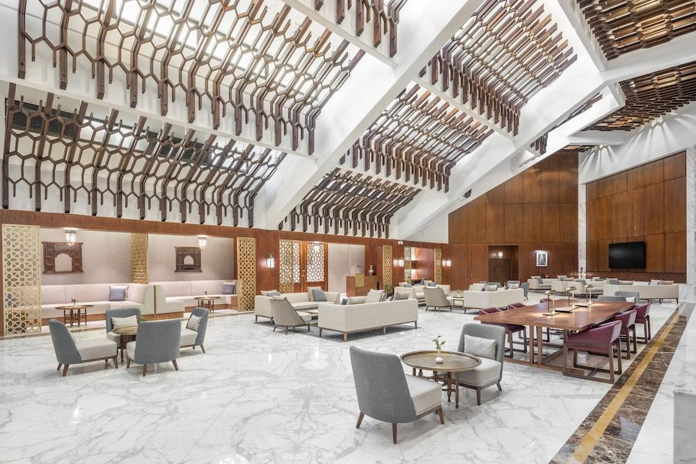 Makarem Ajyad Makkah Hotel Мекка Экстерьер фото The photo shows a spacious and elegantly designed lobby area, likely within a hotel. The interior features high ceilings with a unique architectural design, showcasing wooden elements arranged in a geometric pattern. The flooring is a polished marble