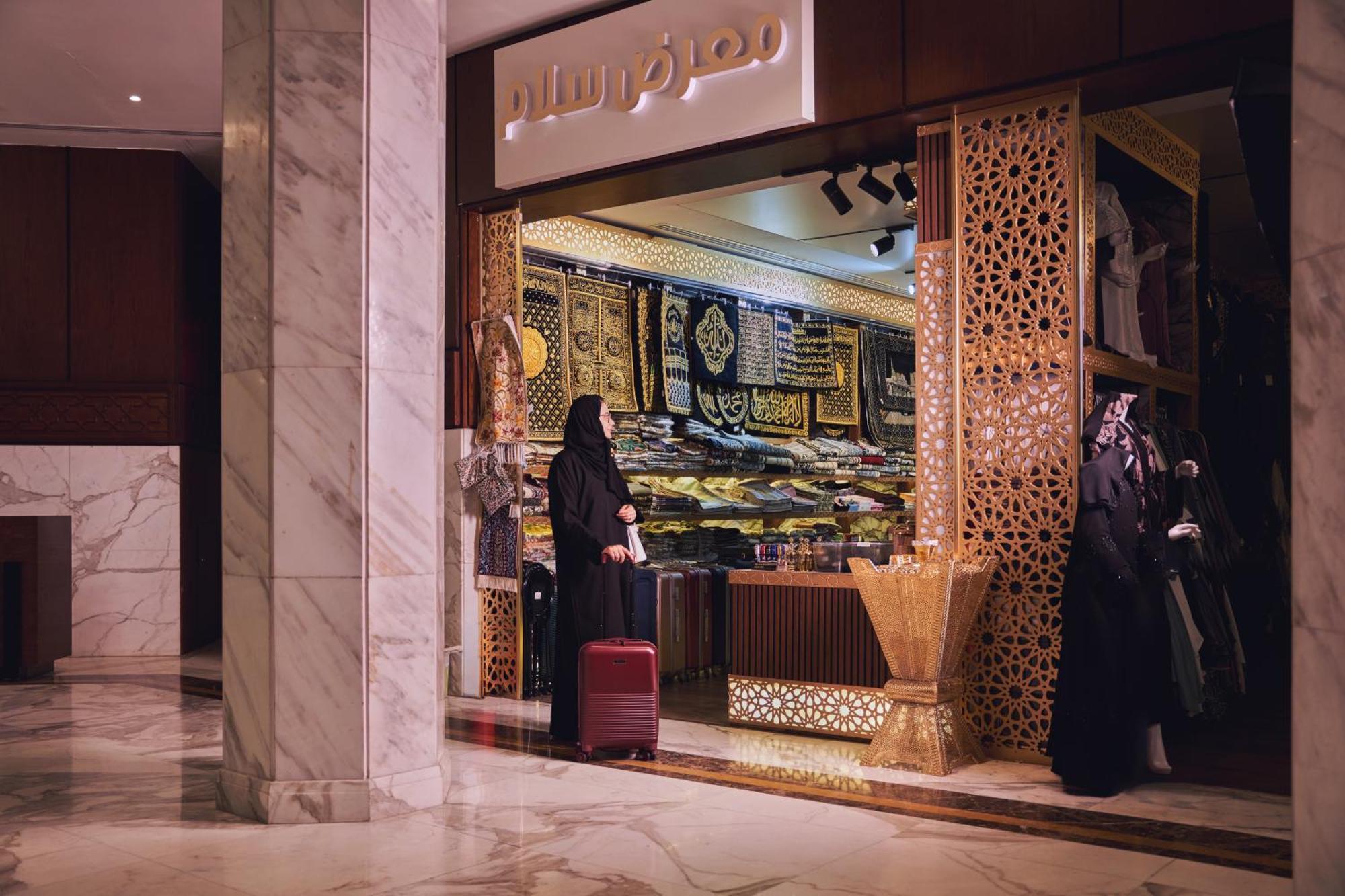 Makarem Ajyad Makkah Hotel Мекка Экстерьер фото The photo shows a storefront that appears to sell traditional textiles or garments. The entrance features intricate decorative patterns, typical of Middle Eastern architecture. A woman is standing outside the shop, dressed in a black abaya, and she h