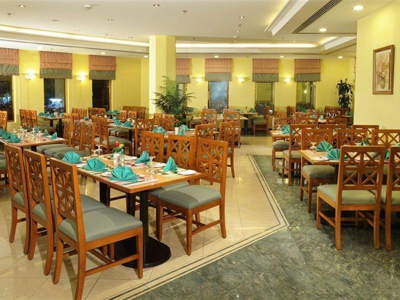 Makarem Ajyad Makkah Hotel Мекка Экстерьер фото The photo shows an interior view of a restaurant. It features wooden tables and chairs arranged neatly throughout the space. Each table is set with turquoise napkins, contributing to the overall decor. The walls are painted a soft yellow, and there a