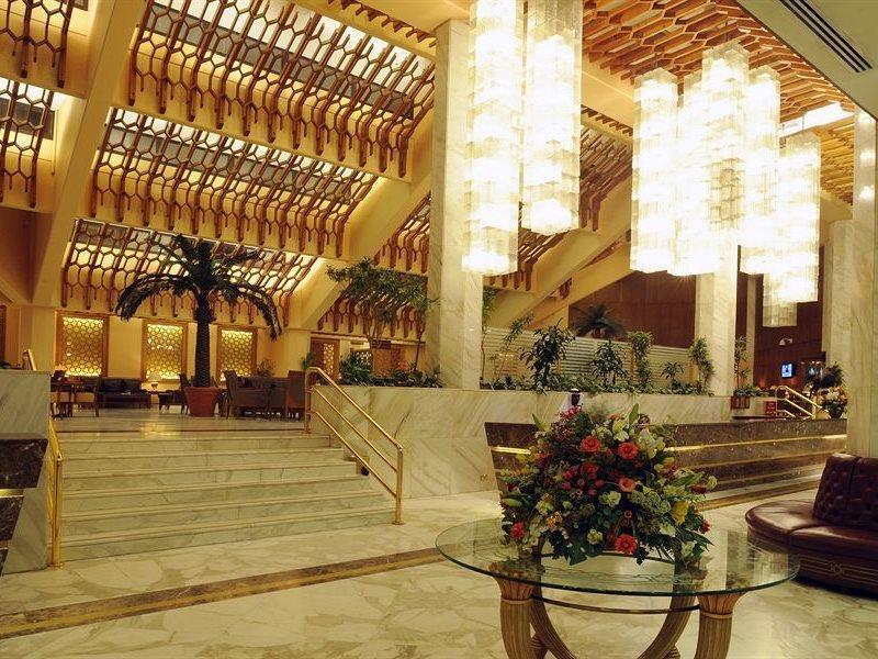 Makarem Ajyad Makkah Hotel Мекка Экстерьер фото The photo shows a luxurious hotel lobby with elegant design features. It has high ceilings adorned with wooden beams and large, decorative light fixtures hanging from above. The lobby is brightly lit, creating a warm and inviting atmosphere. There ar