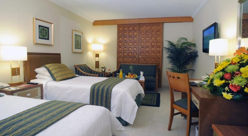 Makarem Ajyad Makkah Hotel Мекка Экстерьер фото The photo shows a hotel room featuring two single beds with white linens and green and blue striped throw blankets. There is a wooden headboard behind the beds and a decorative wooden partition or wall in the background. A cozy seating area is visibl