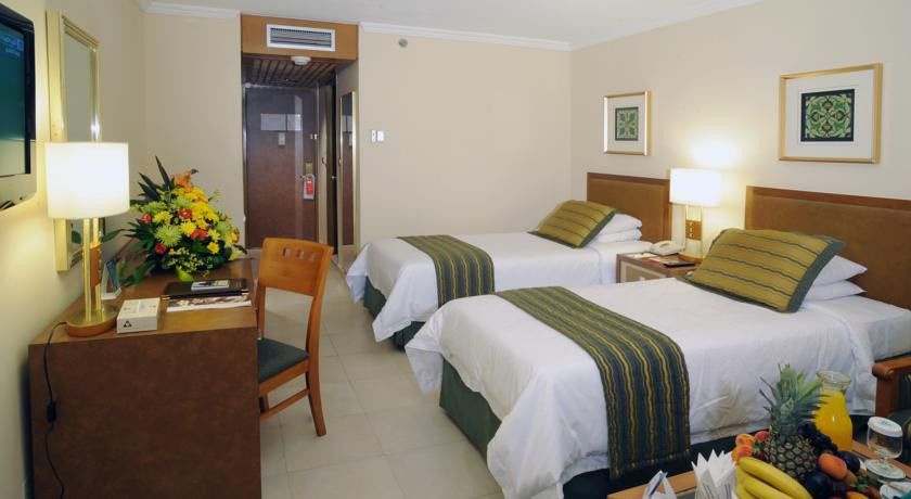 Makarem Ajyad Makkah Hotel Мекка Экстерьер фото The photo shows an interior of a hotel room featuring two twin beds with white linens and green decorative accents. The walls are painted in a light beige color, and there is a small table next to one of the beds. A desk with a chair is positioned ne