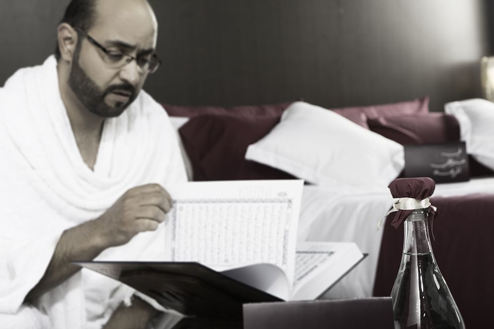 Makarem Ajyad Makkah Hotel Мекка Экстерьер фото The photo shows a man engaged in reading a book or document, seated in a room with a relaxed atmosphere. He is wearing traditional white attire, often associated with specific cultural or religious practices. In the foreground, there is a bottle, pos